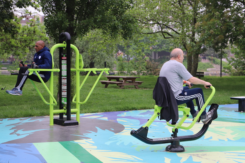 deux hommes pratiquants sur des appareils de fitness installés dans un parc.