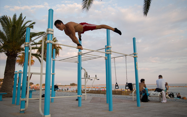 un jeune homme torse nu effectue une planche sur une barre d'un agrès sportif extérieur.