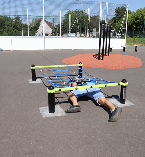 un homme rampe sous un filet sur un espace sportif en plein air.