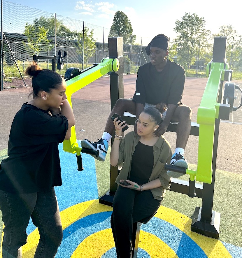 3 adolescents installés sur un appareil de fitness de plein air.