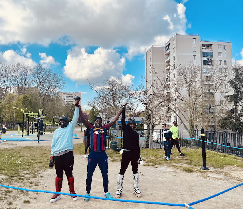 trois hommes souriants sur un ring de boxe installé en extérieur.