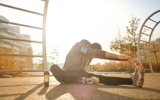 un homme fait des étirements au pieds d'appareil de musculation en plein air.