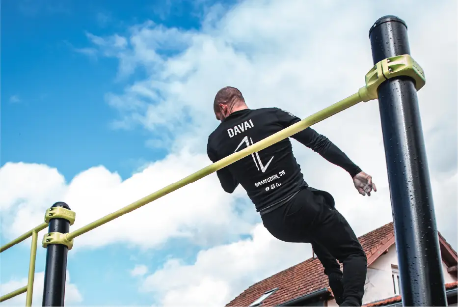 Homme effectuant une rotation 360° sur une barre fixe en plein air avec un ciel bleu.