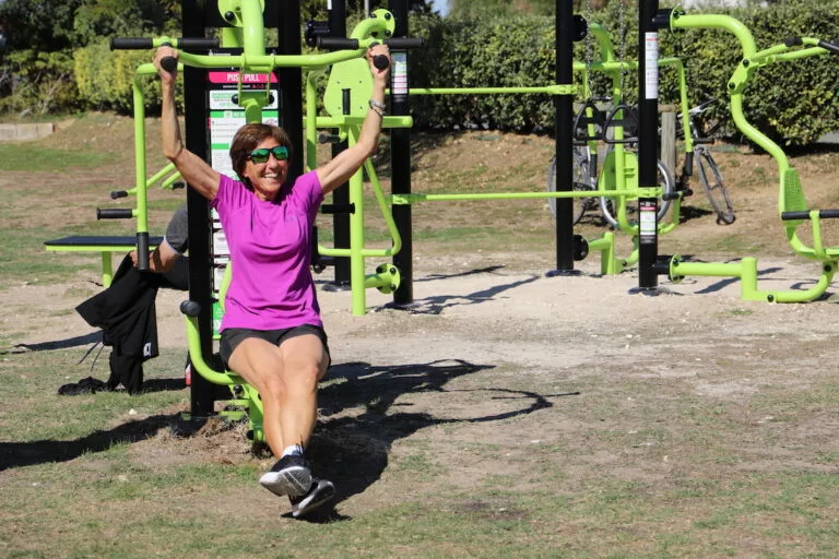 femme agée souriante en train de faire du sport sur une machine de fitness de plein air.